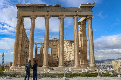 Erechtheion temple Acropolis Athens Greece with two tourists in front and the rooftops of Athens and a beautiful sky in the background