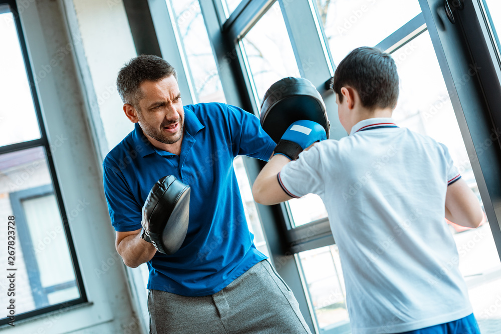 boy in boxing gloves working out with father at gym
