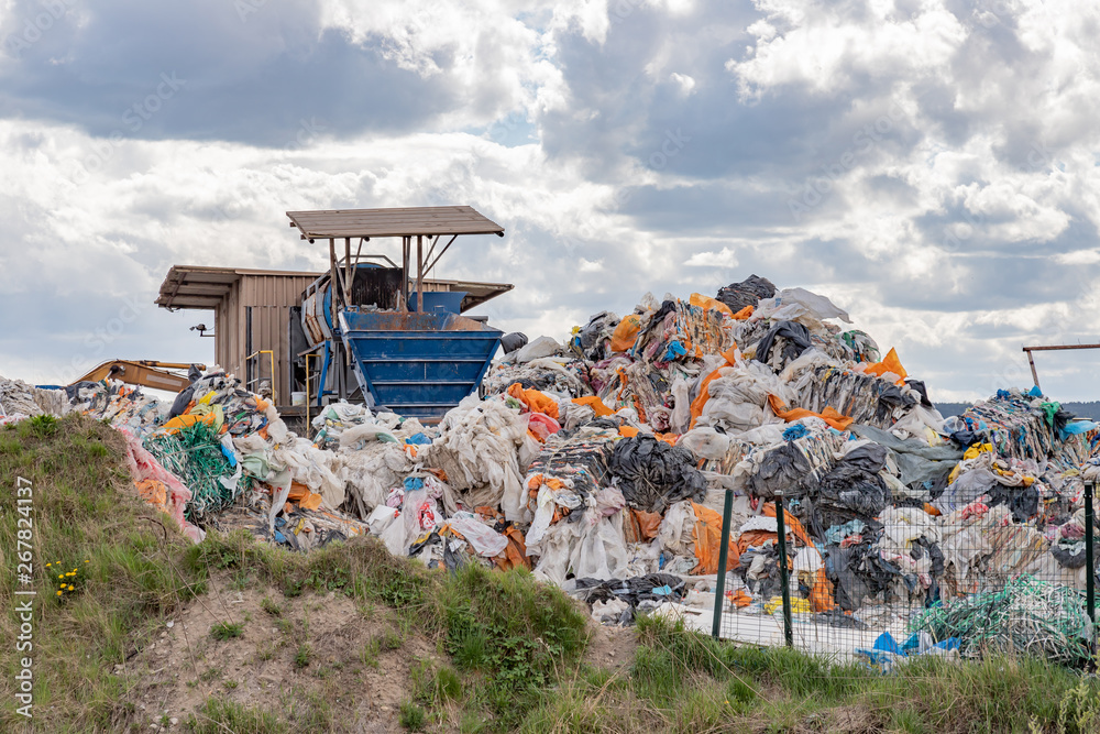 Garbage dump with many colorful garbage, cloudy sky.