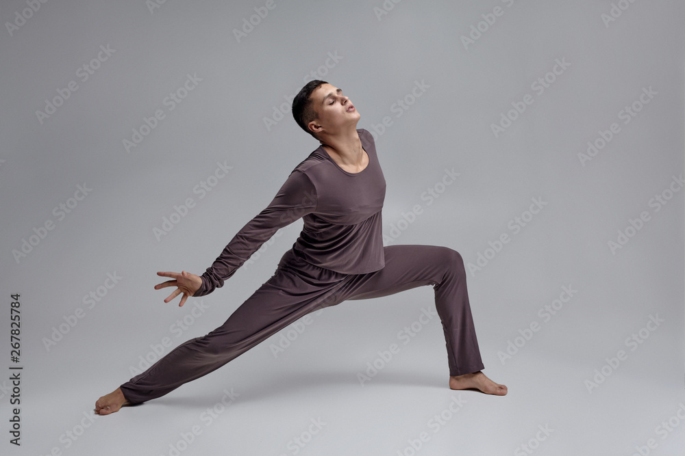 Photo of an athletic man ballet dancer dressed in a gray tracksuit, making a dance element against a gray background in studio. Photo of an athletic man ballet dancer dressed in a gray tracksuit, making a dance element against a gray background in studio.