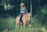 Ein Cowgirl reitet mit ihrem Haflinger und einem Husky durch den Wald