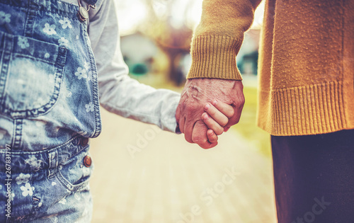Two generations. Old woman and little child holding hands while walking together, close up photo. Family, lifestyle concept