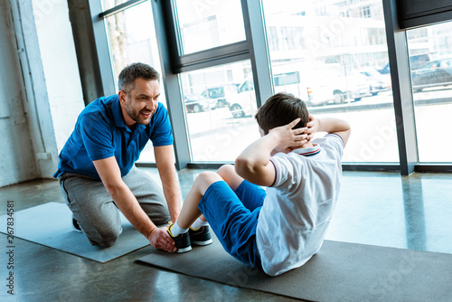 father helping son with sit up exercise at gym