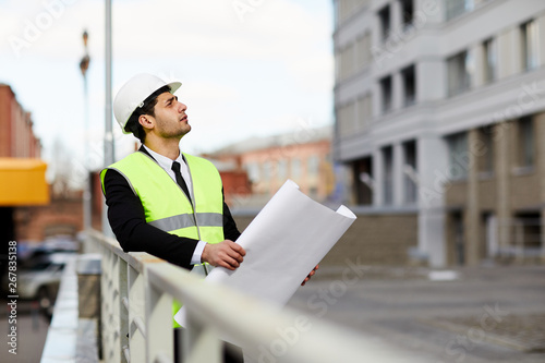 Portrait of Mixed Race engineer holding plans standing at construction site outdoors, copy space