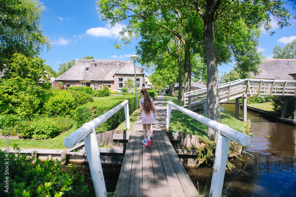 View of famous typical Dutch village Giethoorn with canals. Two girls walk across the bridge. The beautiful Traditional Dutch House and gardening city is know as 