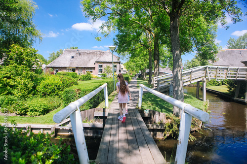 View of famous typical Dutch village Giethoorn with canals. Two girls walk across the bridge. The beautiful Traditional Dutch House and gardening city is know as "Venice of the North".