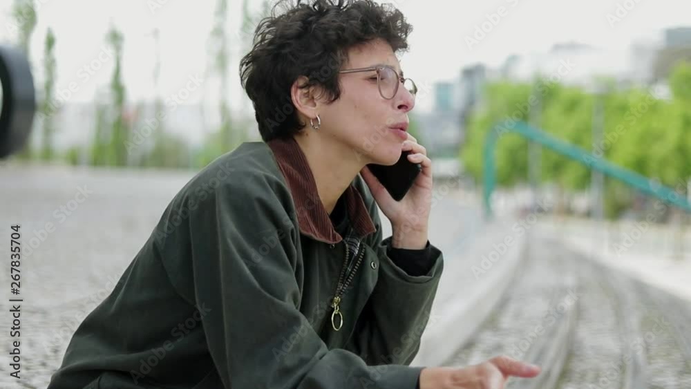 Unhappy woman talking by smartphone on street. Side view of serious woman in eyeglasses having unpleasant phone talk outdoor. Communication concept Unhappy woman talking by smartphone on street. Side view of serious woman in eyeglasses having unpleasant phone talk outdoor. Communication concept