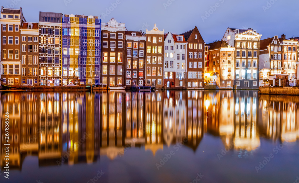 Scenic night view of traditional colourful old houses and boats with reflection on canal Damrak in the old city of Amsterdam, Netherlands.