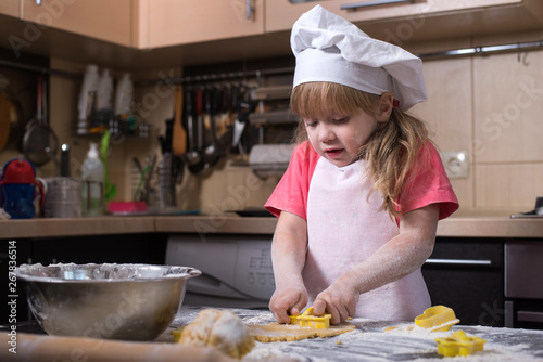 Little baker kid girl in chef hat at kitchen.