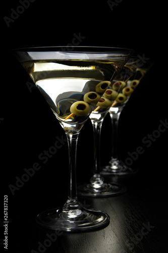 Three Martini drinks with olives on stick isolated on black table