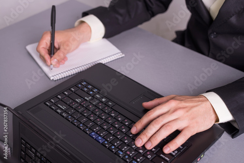 Businessman write in paper documents over the laptop keyboards.