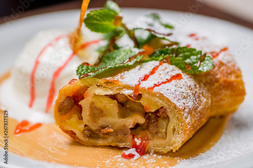 piece of strudel with apples on a white plate with powdered sugar and mint