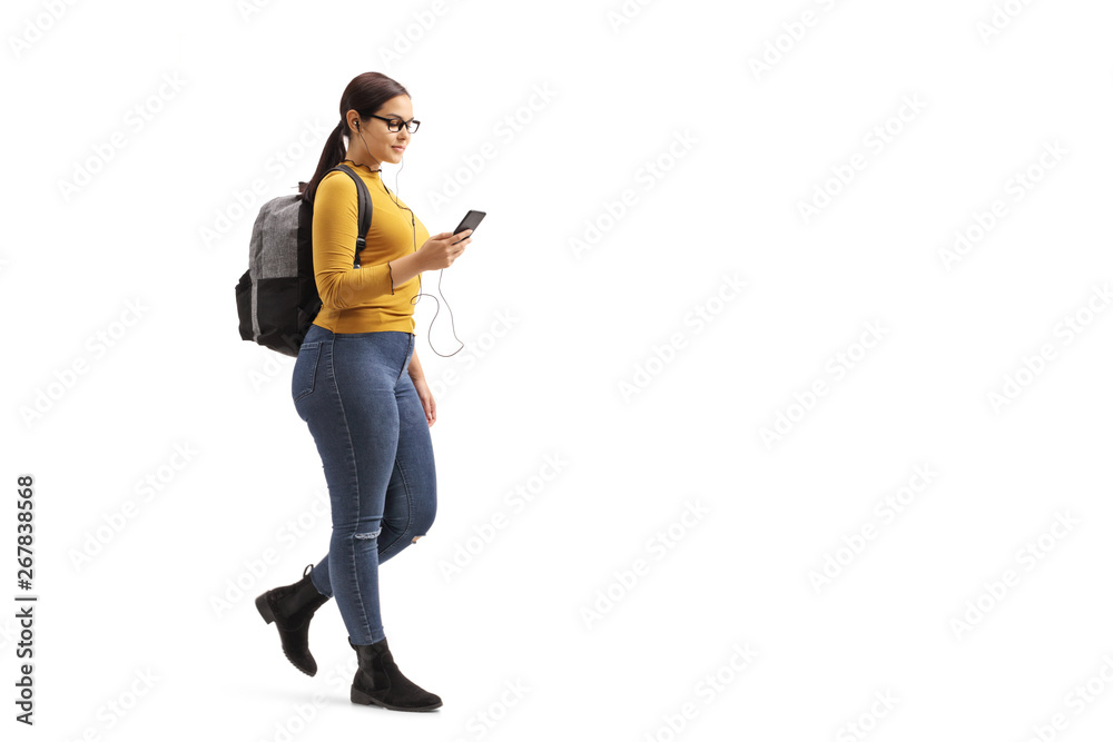 Female student walking and choosing a song from her mobile phone - obrazy, fototapety, plakaty 
