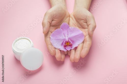 Muscular man hands with natural manicure nails holding orchid flower. Man hands and body skin cosmetic care. White plastic jar with body cream. Mockup for natural herbal man cosmetics.