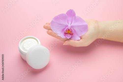 Mockup for body skin care natural cosmetics. Woman hold orchid flower in hand on a pink background. Natural organic cosmetics with flowers extract. Beauty, fashion, cosmetology and spa concept.
