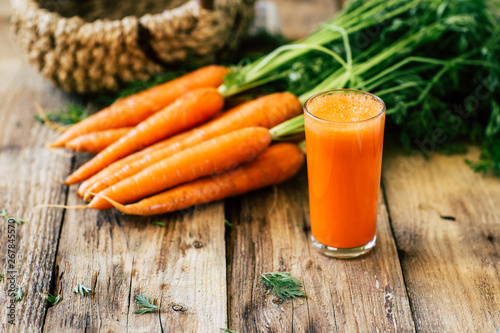 Fresh carrots with stem and leaves on a wooden background, carrot juice, vegetables harvest