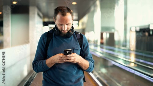 Man, tourist texting on smartphone riding escalator stairs at airport