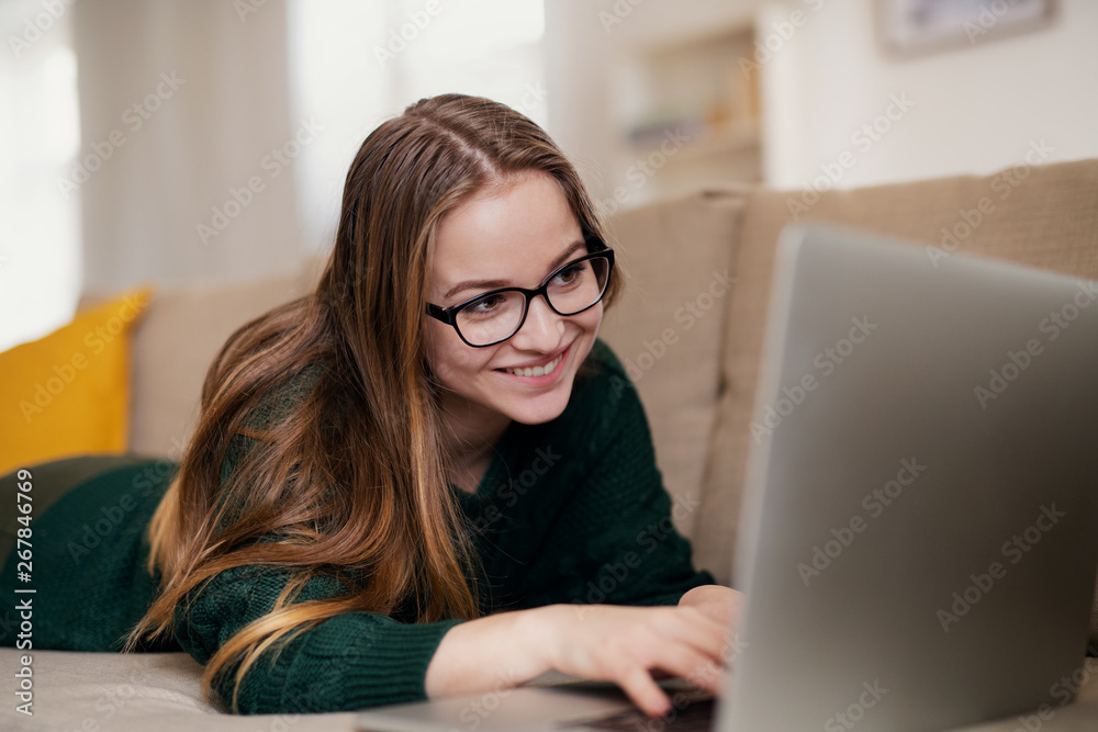 A young female student lying on sofa, using laptop when studying. A young female student lying on sofa, using laptop when studying.