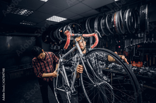 Two attractive mans are working on bicycle fixing at busy workshop.