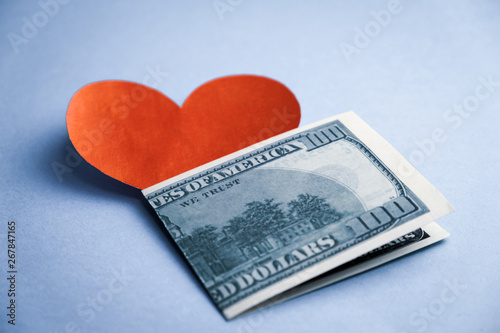 Red heart shape and 100 dollar bills on blue background.