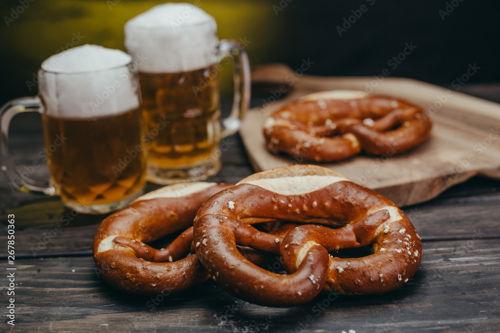 draft beer in the mugs and pretzels on dark wooden background