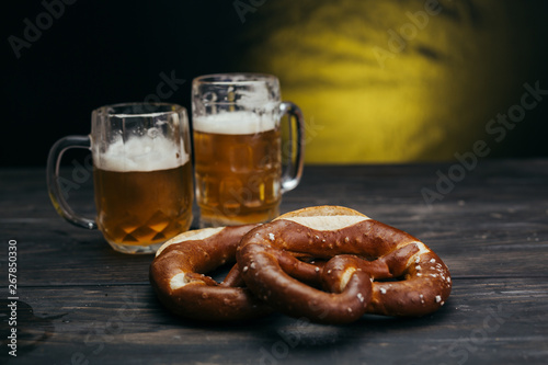 draft beer in the mugs and pretzels on dark wooden background