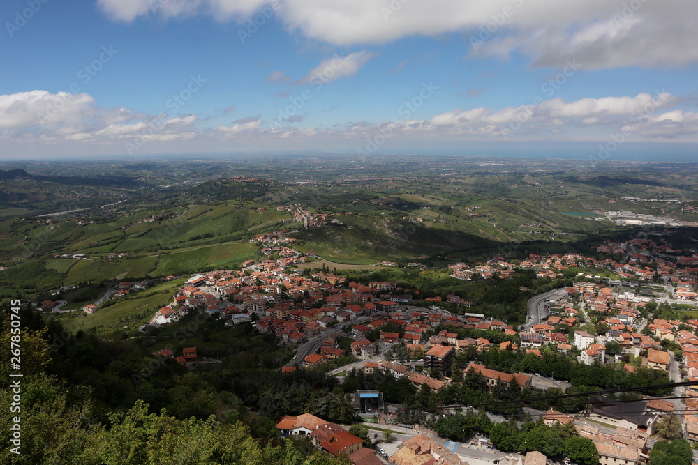 panoramic view from top of Fortress Guaita on Mount Titano on city San Marino ,Italy with beautiful blue sky with clouds on sunny day. View towards the sea and over the San Marino villages and Rimini,