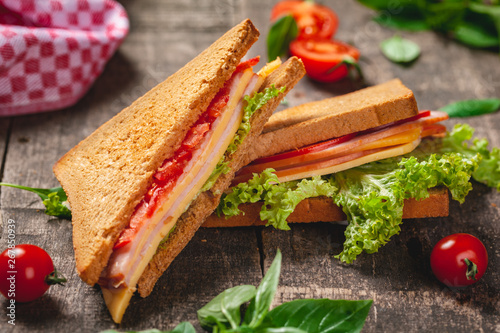 Sandwich with ham, cheese, tomatoes and lettuce leaves on wooden rustic table. Close up