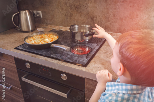 Child reaches for the hot electric stove. Child safety at the kitchen.