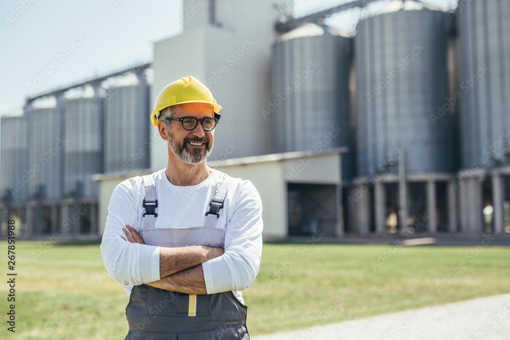 middle aged agricultural worker standing crossed arms in front of grain silo - obrazy, fototapety, plakaty 