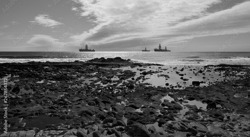 Rocky coast at low tide, oil platforms and cloudy sky, black and white mode 