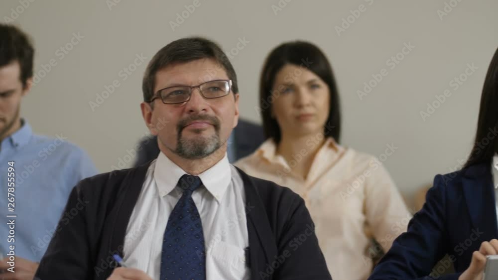 Close up portrait of diverse multi ethnic audience sitting and listening to public speaker at business seminar. Attentive business people writing notes while business coach giving a speech Close up portrait of diverse multi ethnic audience sitting and listening to public speaker at business seminar. Attentive business people writing notes while business coach giving a speech