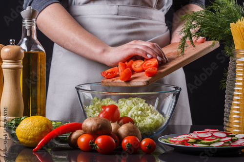 young woman in a gray apron adds cherry tomatoes to a salad