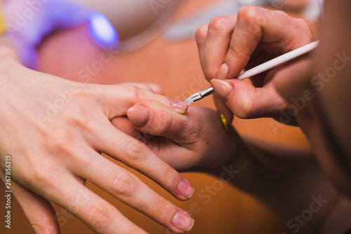 A woman applies gel polish on her nails with a thin brush. Salon procedures at home. close-up