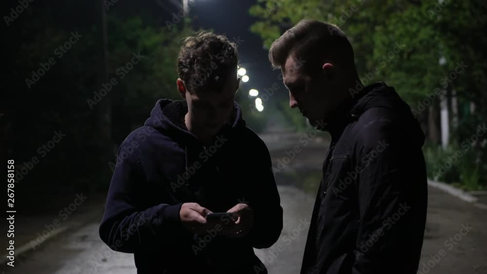 Young boys laughing from funny video on smartphone. Friends using phone on the street at night Young boys laughing from funny video on smartphone. Friends using phone on the street at night