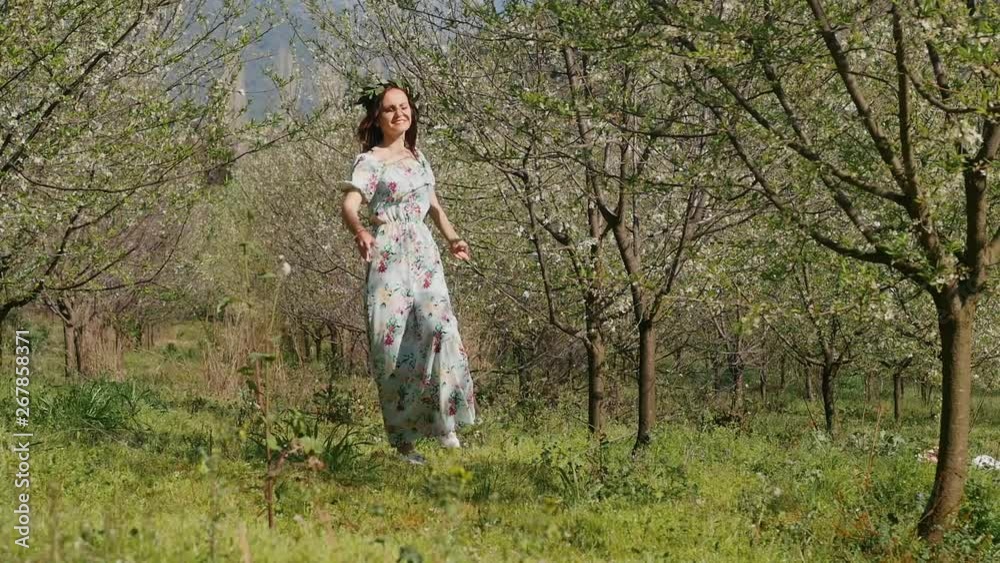 Young beautiful woman in long dress walking in spring blossom garden Young beautiful woman in long dress walking in spring blossom garden