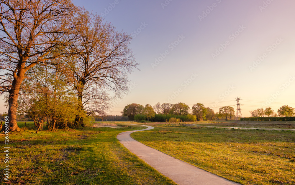 Sweeping bicycle trail in a Dutch farm landscape during sunset. It is located near the small neighbourhood called Tusveld, near the town of Almelo in the Eastern Netherlands.