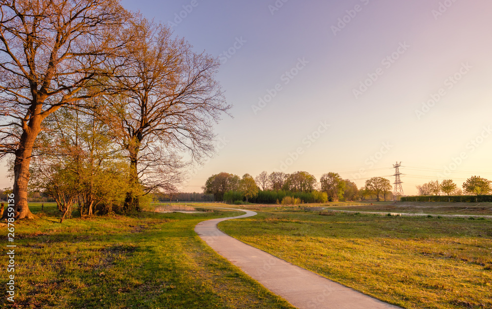 Fototapeta premium Sweeping bicycle trail in a Dutch farm landscape during sunset. It is located near the small neighbourhood called Tusveld, near the town of Almelo in the Eastern Netherlands.