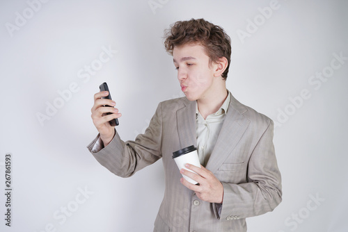 funny emotional teen boy standing with paper cup of tea and doing selfie on white background alone