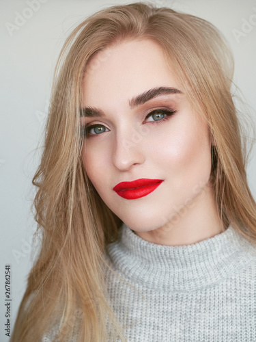 Closeup natural light beauty portrait of blonde woman model with vibrant saturated red lips bright lips makeup, cheekbones and healthy shiny skin.