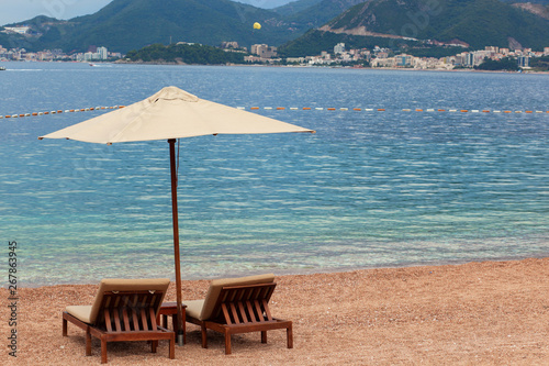 Adriatic sea summer beach. Wooden chairs and umbrella on pebble beach by blue water. Montenegro, Budva riviera