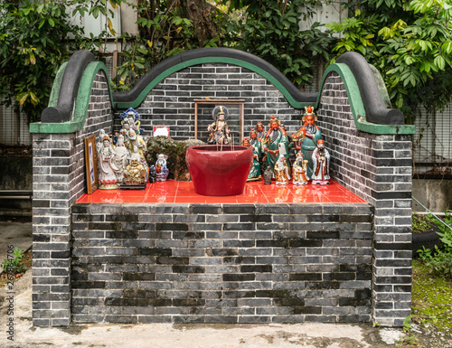 Hong Kong, China - March 8, 2019: Tung Shan Temple in Wing Ping Tsuen Neighborhood. Small shrine on courtyard for Matzu, Goddess of the sea, with images of red-face Kwan. God of War. Greem foliage. photo