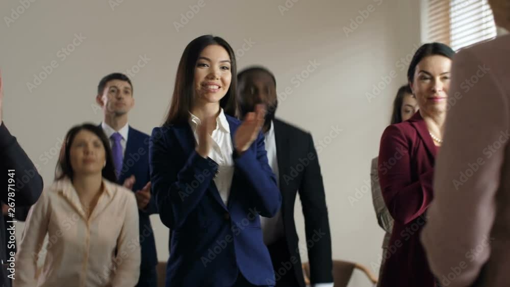 Smiling diverse multieraced business colleagues getting up and cheering greeting department director blurry back to waist on foreground. SAudience of co-workers ready for corporate training Smiling diverse multieraced business colleagues getting up and cheering greeting department director blurry back to waist on foreground. SAudience of co-workers ready for corporate training