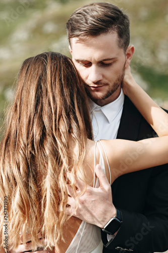 Portrait of a confident handsome groom embracing his bride with closed eyes outside in their wedding day. photo
