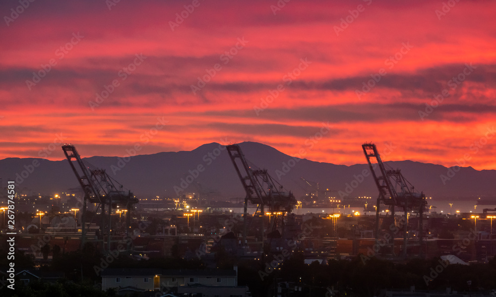 Sunrise over the Port of Los Angeles in San Pedro, California, Novermber 2018, with red orange color of smoke from Woolsey fire with large giant cranes and San Bernardino mountains in background.