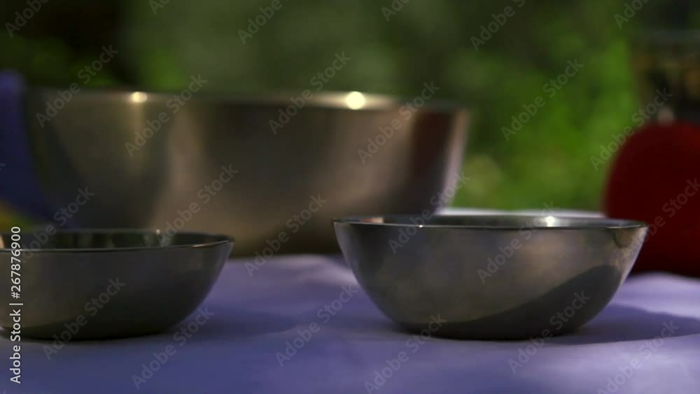 traditional bronze tibetan bowls are standing on table in open air, master is hitting by mallet