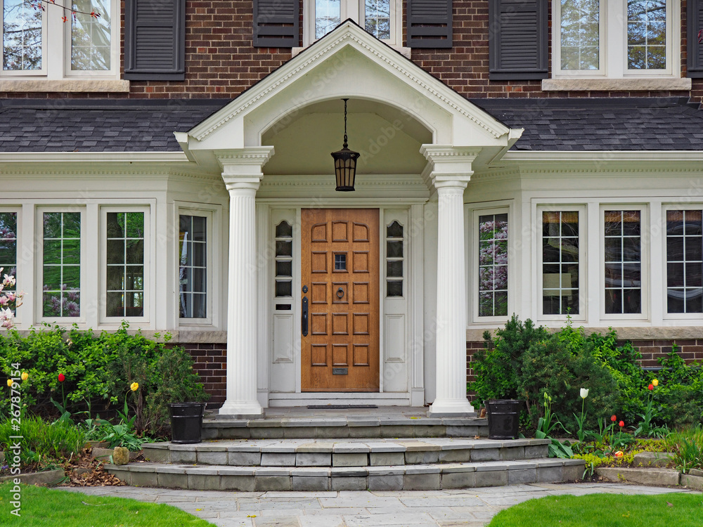 elegant wooden front door of large suburban house with gabled portico - obrazy, fototapety, plakaty 