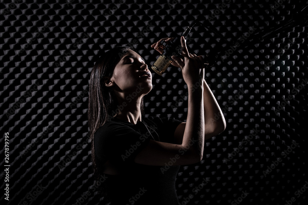 Asian Adult Woman sing a song loudly with power sound over hanging  microphone condenser filter in black shirt. Egg Crate Studio lighting  shadow silhouette Sound Proof Absorbing wall room Stock Photo |