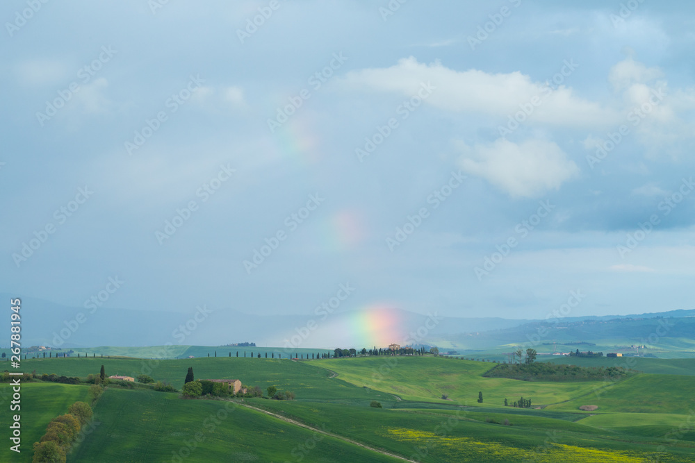 Hills with rainbow.. Val d'Orcia landscape in spring. Hills of Tuscany. Cypresses, hills, yellow rapeseed fields and green meadows. Val d'Orcia, Siena, Tuscany, Italy - May, 2019.