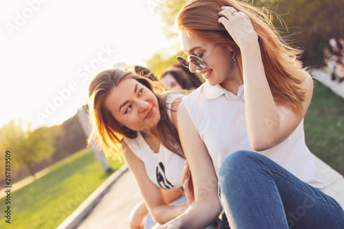 Positive beautiful happy red haired girl in mirror sunglasses with friends on city street background, summer sunset time